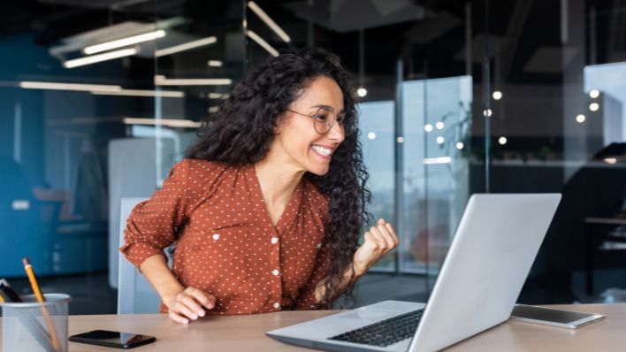 Una persona de negocios celebrando el éxito mientras trabaja en su computadora portátil.
