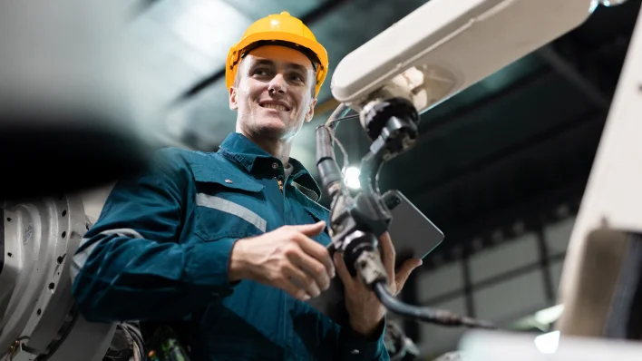 Male emerging technologies worker in hardhat holding robotic arm