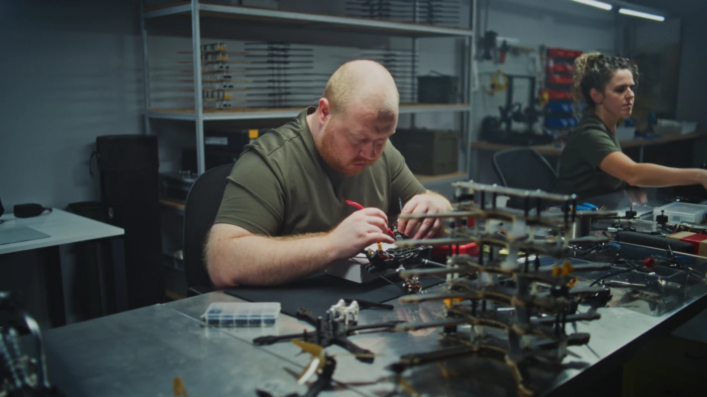 Two people performing assembly jobs in an industrial warehouse setting.