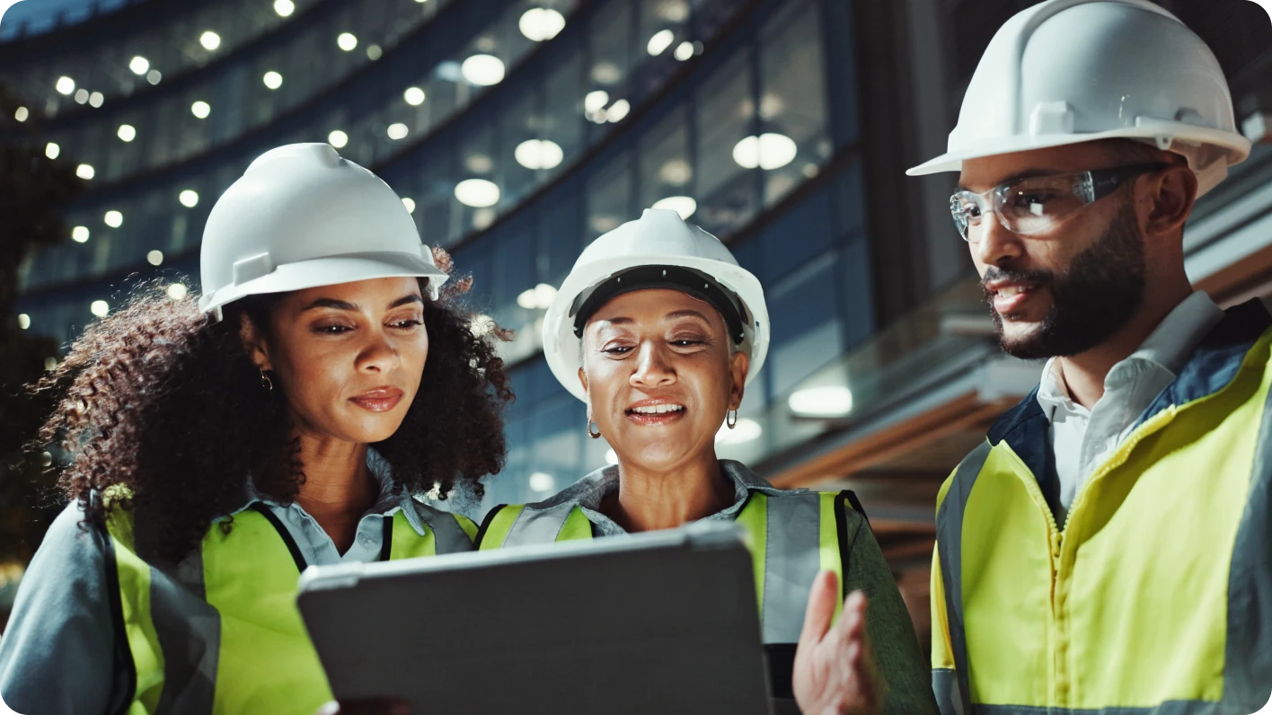 Tres trabajadores afroamericanos jóvenes observando una pantalla de computadora portátil en un entorno de fábrica.
