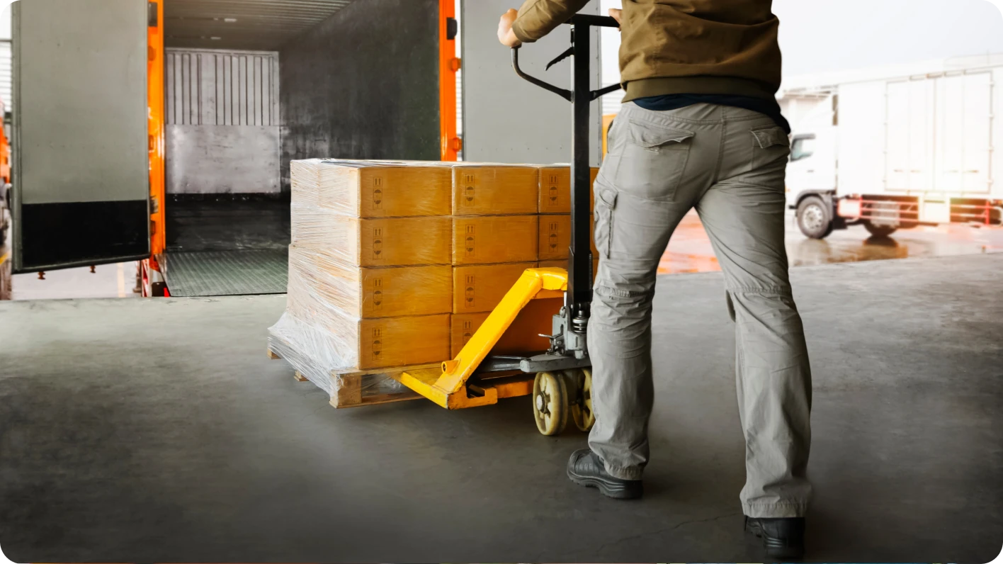A male general laborer, shown from neck down, loads a pallet of boxes into a truck.