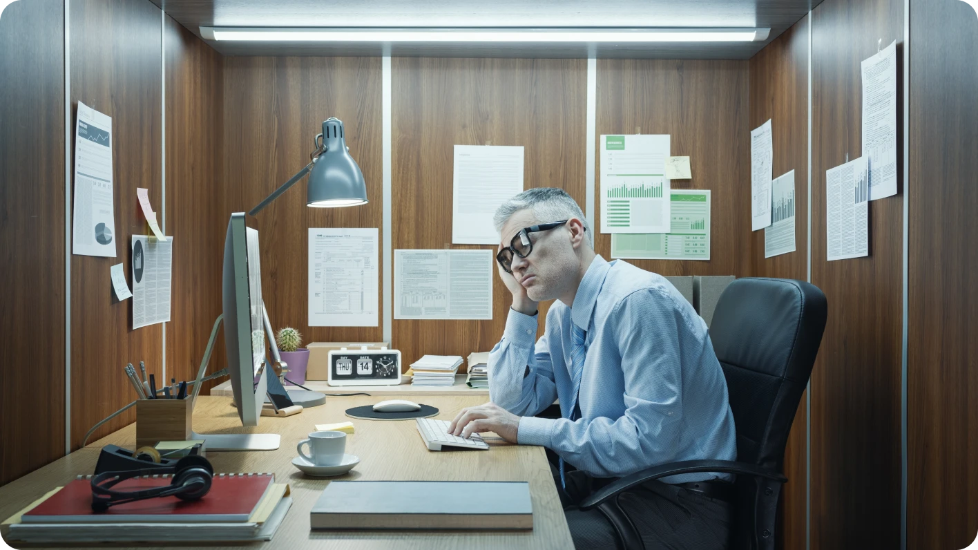 Job-hugging white male with graying hair sits in a tiny office. He slumps in his chair, looks halfheartedly at a computer screen.